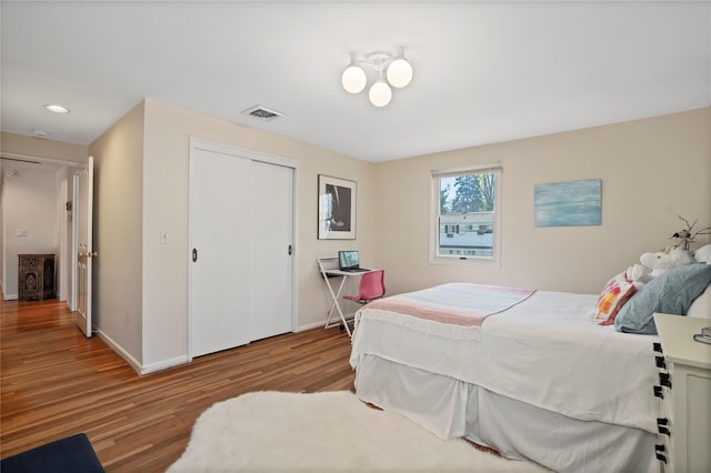 bedroom with a closet, visible vents, wood finished floors, and baseboards