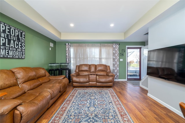 living room featuring a tray ceiling, recessed lighting, wood finished floors, and baseboards