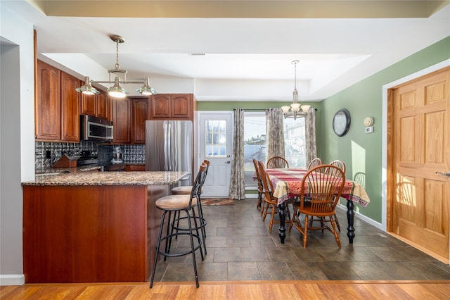 kitchen featuring stainless steel appliances, a peninsula, a kitchen breakfast bar, hanging light fixtures, and backsplash