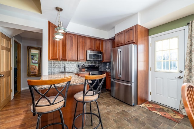 kitchen with stone counters, a sink, appliances with stainless steel finishes, backsplash, and pendant lighting