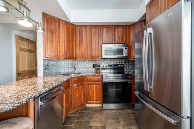 kitchen featuring tasteful backsplash, hanging light fixtures, light stone countertops, stainless steel appliances, and a sink