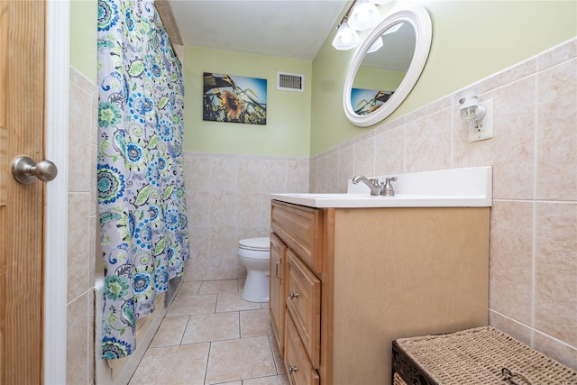 bathroom featuring visible vents, toilet, tile patterned floors, vanity, and tile walls