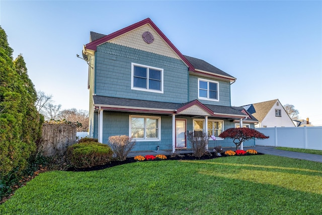 view of front of property with a front yard, covered porch, roof with shingles, and fence