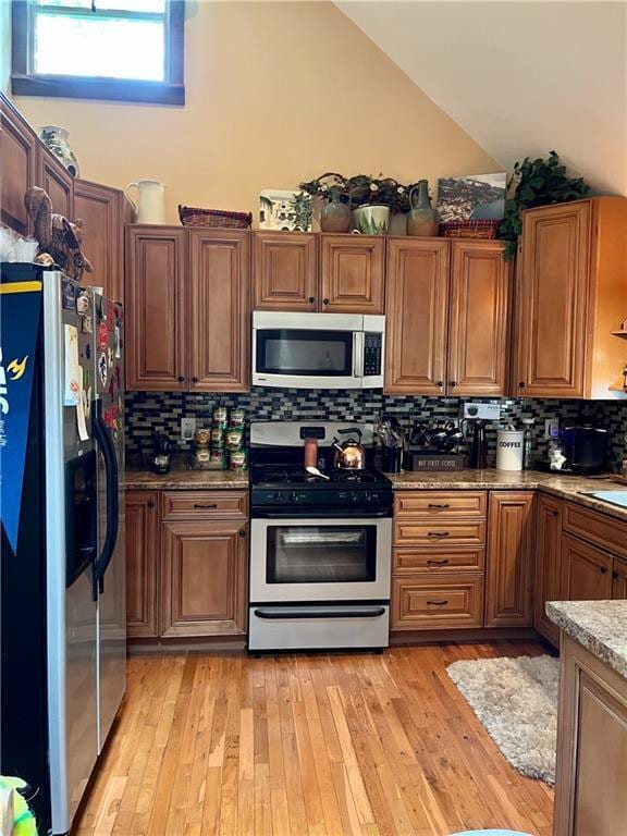 kitchen with light wood-type flooring, appliances with stainless steel finishes, stone counters, and tasteful backsplash