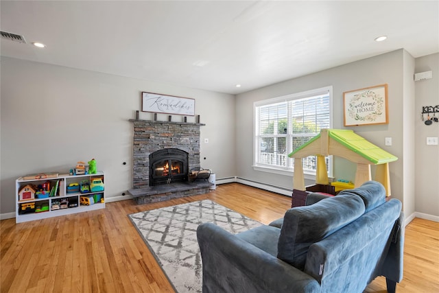 living room featuring hardwood / wood-style floors, a baseboard heating unit, and a stone fireplace