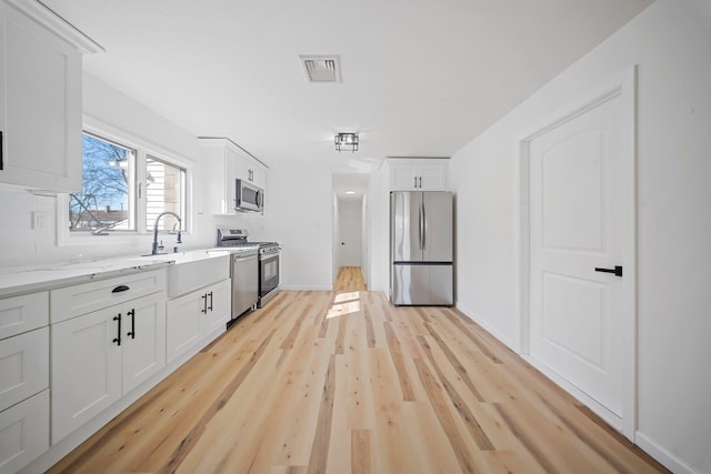 kitchen featuring appliances with stainless steel finishes, sink, light stone counters, white cabinetry, and light hardwood / wood-style floors