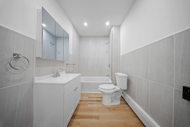 full bathroom with toilet, tile walls, vanity, hardwood / wood-style floors, and tiled shower / bath combo