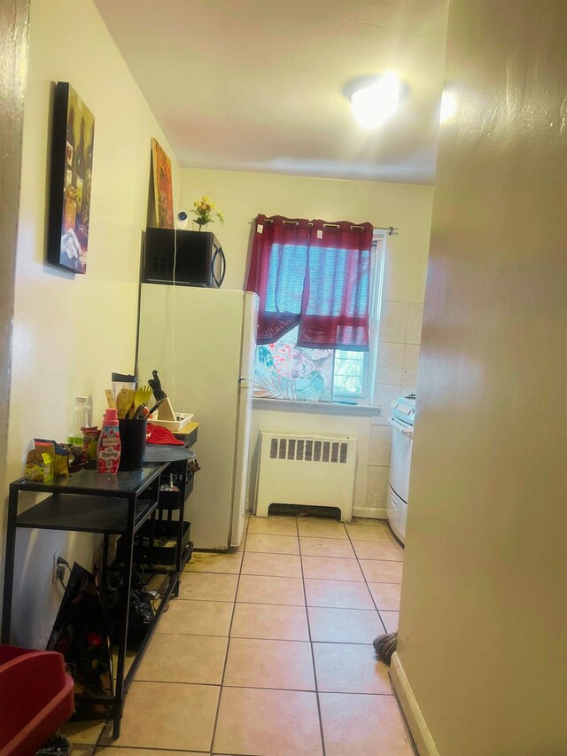 kitchen featuring radiator, light tile patterned floors, and white appliances