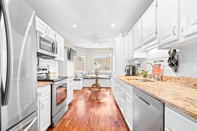 kitchen with light stone counters, stainless steel appliances, light wood-style floors, white cabinets, and a sink