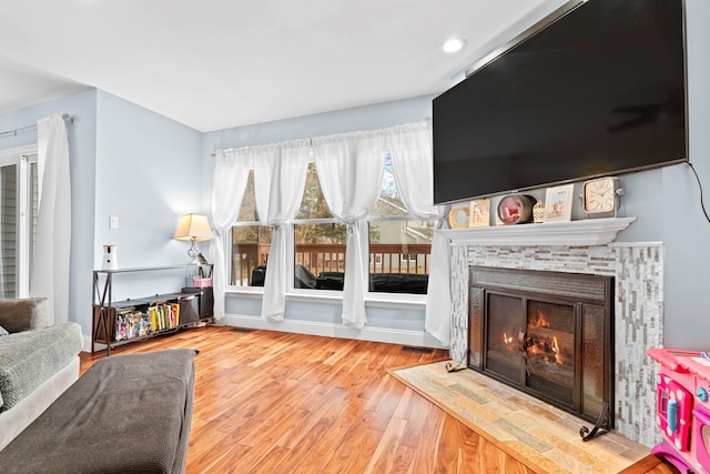 living room featuring a warm lit fireplace, visible vents, and wood finished floors