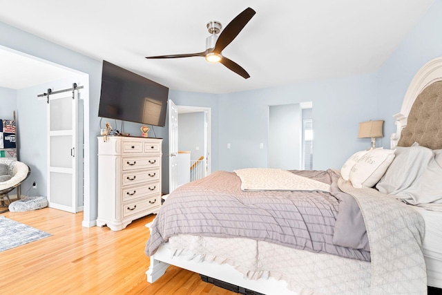 bedroom featuring a barn door, ceiling fan, and wood finished floors