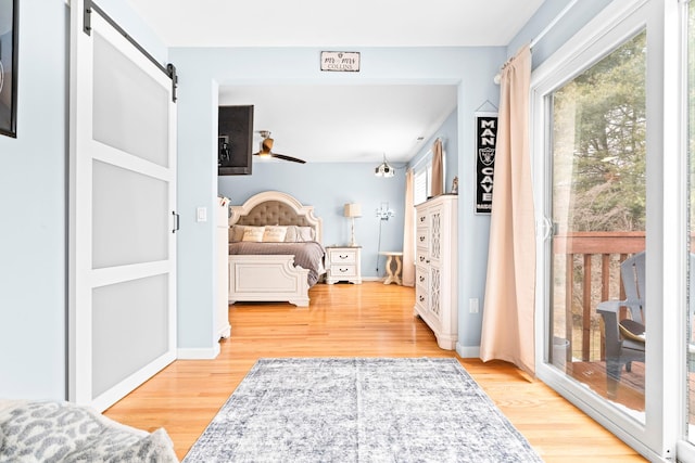 bedroom featuring a barn door, multiple windows, access to outside, and light wood-style flooring