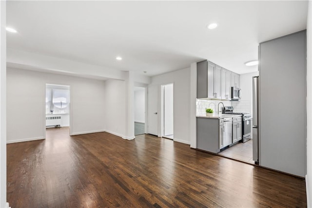 kitchen featuring appliances with stainless steel finishes, radiator, tasteful backsplash, gray cabinetry, and hardwood / wood-style floors