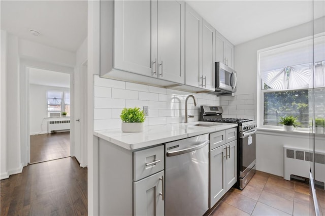 kitchen featuring appliances with stainless steel finishes, a sink, backsplash, and radiator heating unit