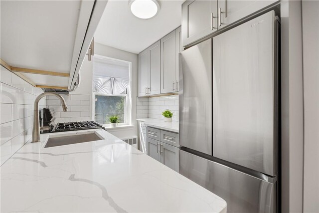 kitchen featuring a sink, backsplash, stainless steel fridge, and gray cabinetry