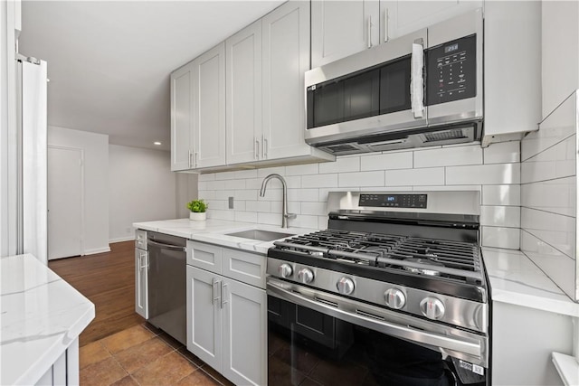 kitchen featuring tasteful backsplash, appliances with stainless steel finishes, light stone counters, and a sink