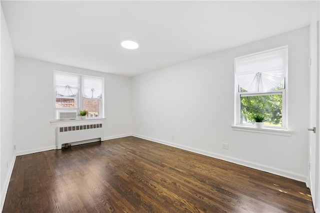 spare room featuring dark wood-style floors, radiator heating unit, and baseboards