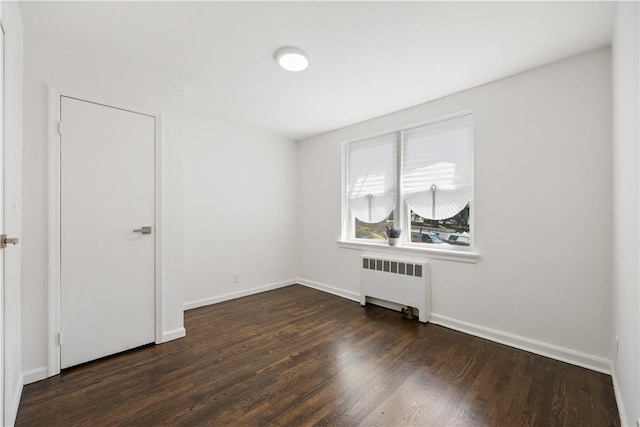 empty room featuring baseboards, dark wood-type flooring, and radiator