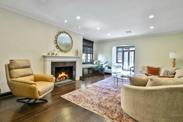 living area featuring recessed lighting, arched walkways, a high end fireplace, dark wood-type flooring, and crown molding