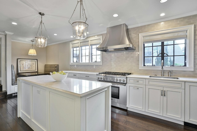 kitchen with high end stove, a sink, a kitchen island, wall chimney exhaust hood, and crown molding