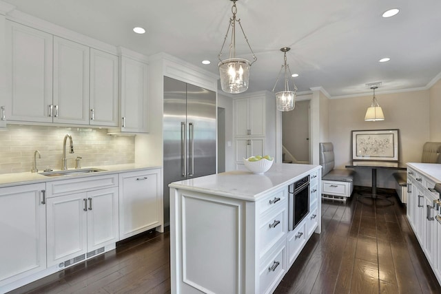 kitchen with white cabinets, built in refrigerator, light countertops, and a sink