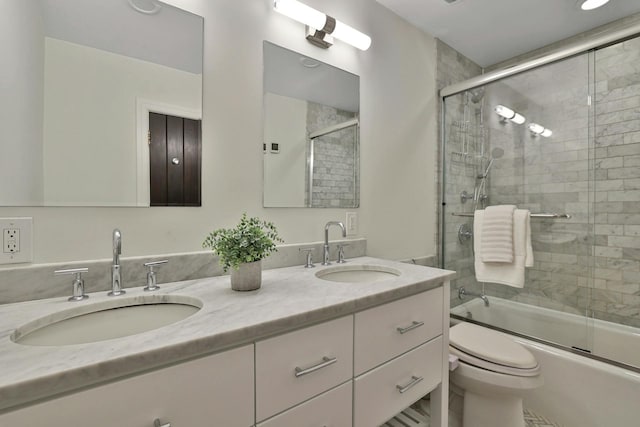 bathroom featuring a sink, bath / shower combo with glass door, double vanity, and toilet