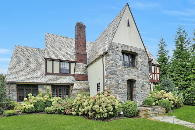 english style home with stone siding, stucco siding, a chimney, and a high end roof