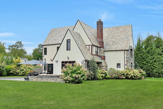 back of property with a high end roof, stucco siding, a chimney, and stone siding