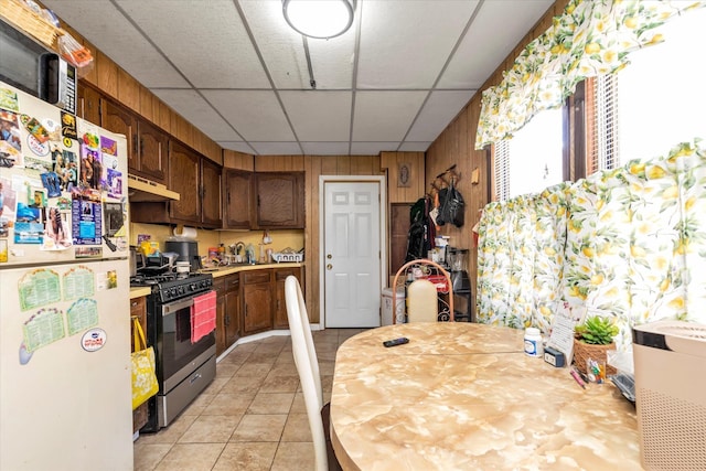 kitchen featuring freestanding refrigerator, light countertops, a paneled ceiling, under cabinet range hood, and gas stove