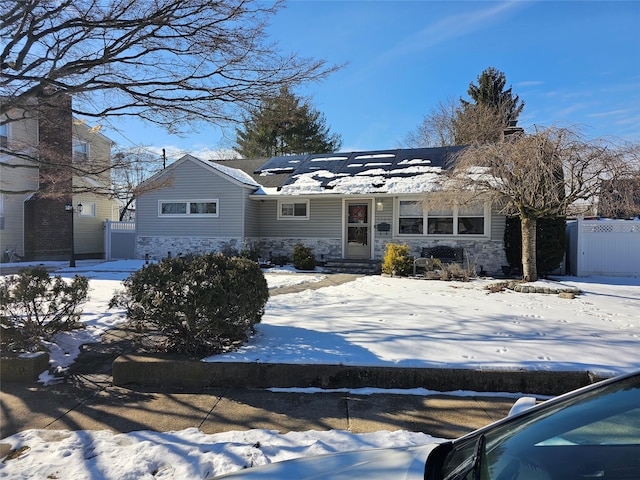 ranch-style house featuring stone siding, solar panels, and fence