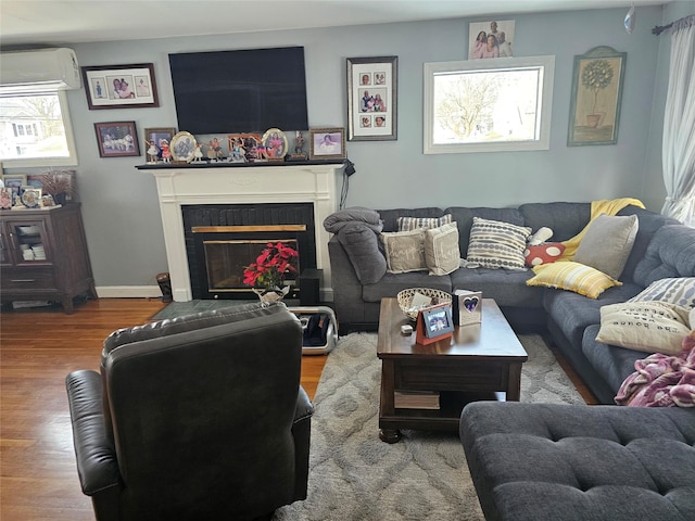 living room with wood finished floors, a wall mounted AC, a glass covered fireplace, and baseboards