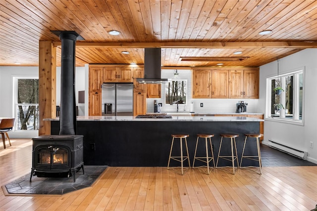 kitchen featuring island exhaust hood, a baseboard radiator, appliances with stainless steel finishes, a wood stove, and wood finished floors