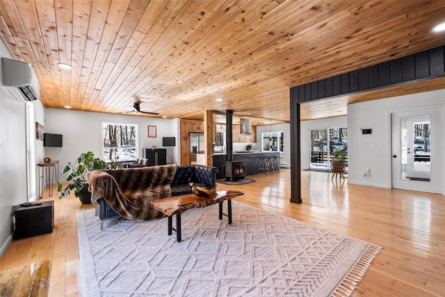 living area featuring ceiling fan, wooden ceiling, light wood-style floors, a wall mounted AC, and a wood stove