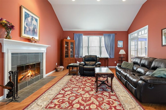 living area with lofted ceiling, baseboards, a tiled fireplace, and wood finished floors