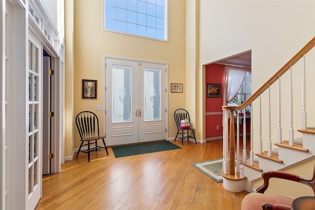 entryway with wood finished floors, a towering ceiling, baseboards, french doors, and stairway