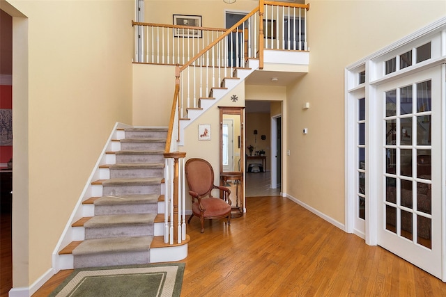 stairway with wood finished floors, baseboards, and a high ceiling
