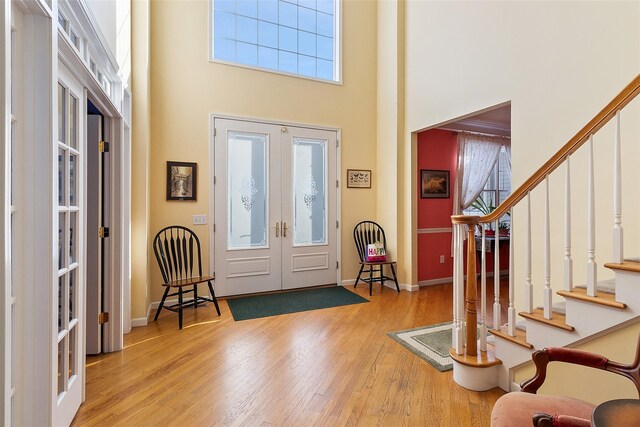 entryway featuring french doors, a towering ceiling, wood finished floors, stairway, and baseboards