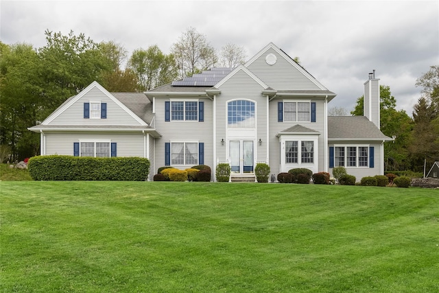 colonial inspired home featuring solar panels, a front yard, and a chimney