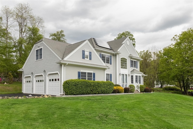 view of front facade with roof mounted solar panels, an attached garage, a front lawn, and driveway