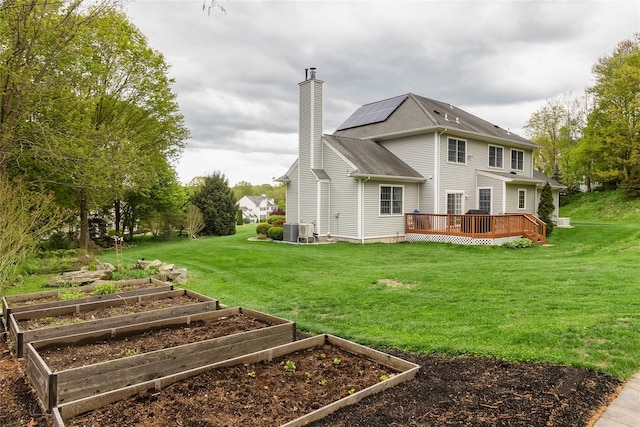 back of property featuring a garden, a chimney, cooling unit, a lawn, and a deck