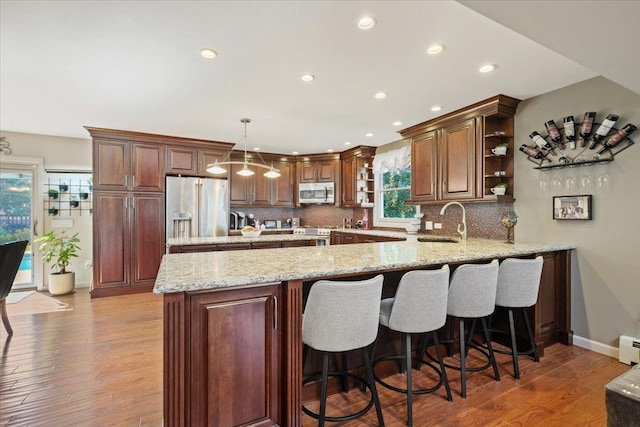 kitchen with open shelves, stainless steel appliances, hanging light fixtures, a sink, and a peninsula