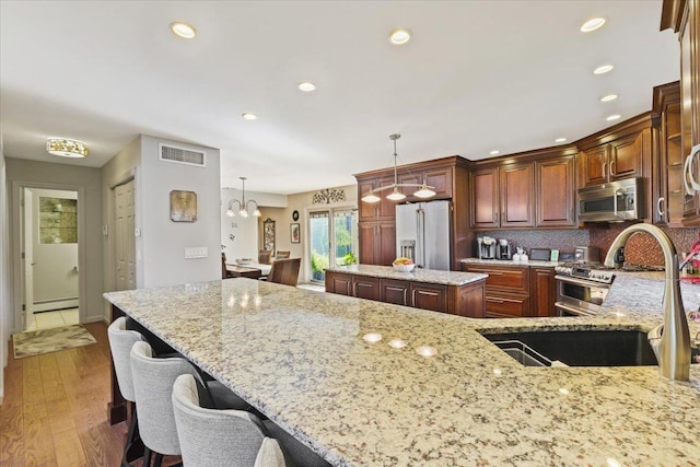 kitchen with premium appliances, a center island, pendant lighting, visible vents, and light stone countertops