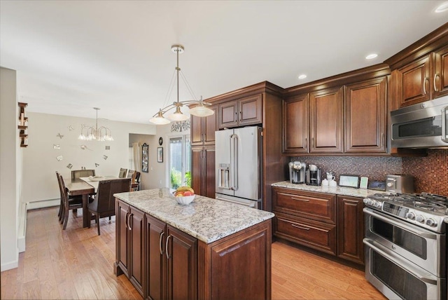 kitchen with light wood-style flooring, light stone countertops, hanging light fixtures, appliances with stainless steel finishes, and decorative backsplash