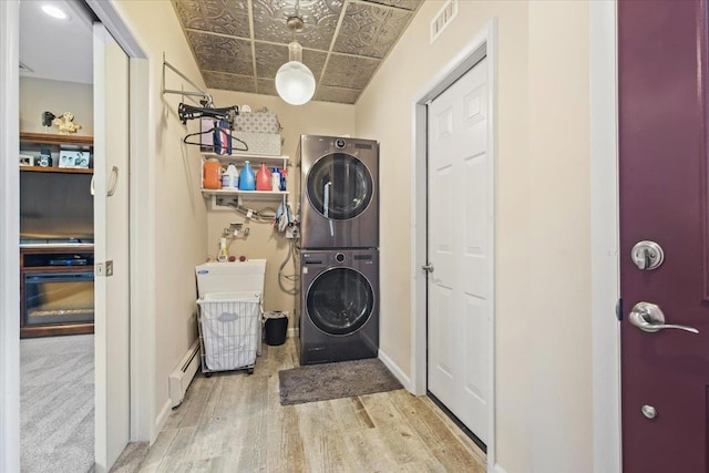 clothes washing area with visible vents, baseboard heating, light wood-style floors, stacked washer / dryer, and laundry area