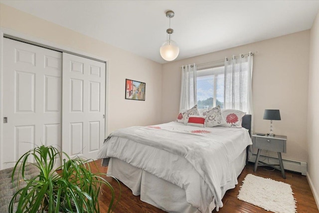 bedroom featuring baseboards, dark wood-style flooring, baseboard heating, and a closet