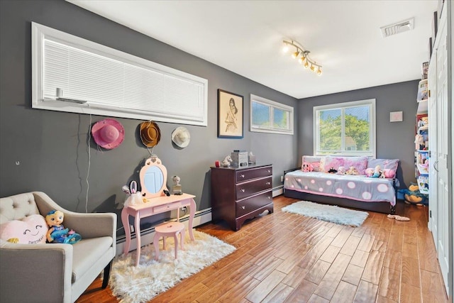 bedroom with a baseboard heating unit, visible vents, and light wood finished floors