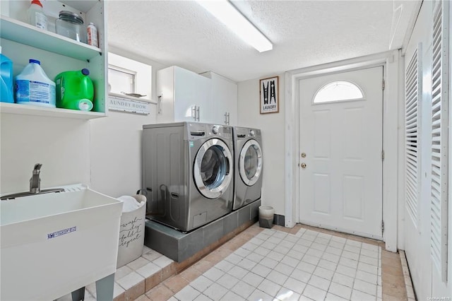 clothes washing area with cabinets, washing machine and clothes dryer, sink, light tile patterned floors, and a textured ceiling