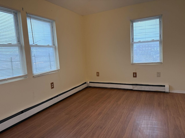 spare room with baseboard heating, wood finished floors, and baseboards