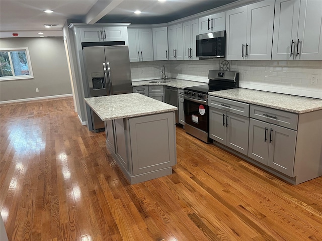 kitchen featuring gray cabinets, a center island, stainless steel appliances, and light stone countertops