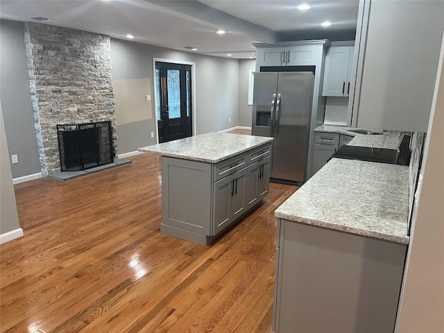 kitchen with a fireplace, gray cabinetry, a center island, stainless steel refrigerator with ice dispenser, and light hardwood / wood-style floors